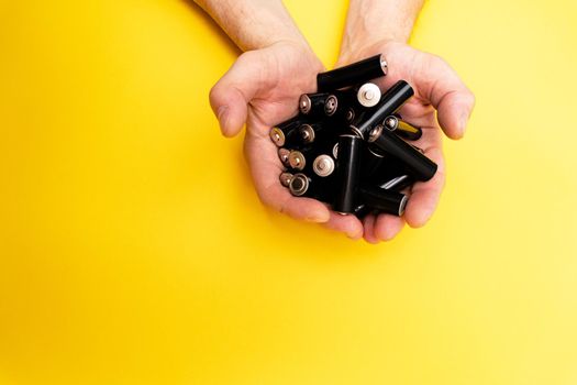 A lot of black aa batteries in male hands on yellow background, view from the top, minimal concept, copy space.