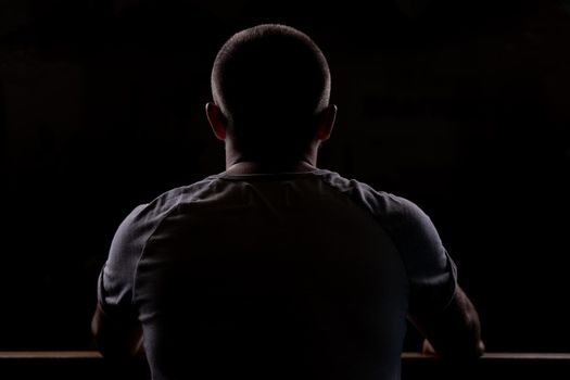 Silhouette of a young guy who sits. Close-up view from behind. Backlight.
