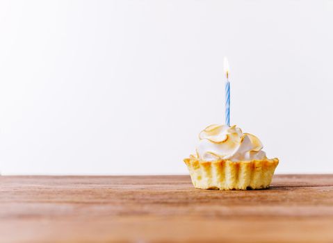 Birthday delicious cupcake with burning candle on a wooden table. Copy-space in left part of image.