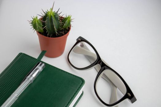 Office desk with glasses, cactus pot and notebook with pen. Top view with copy space