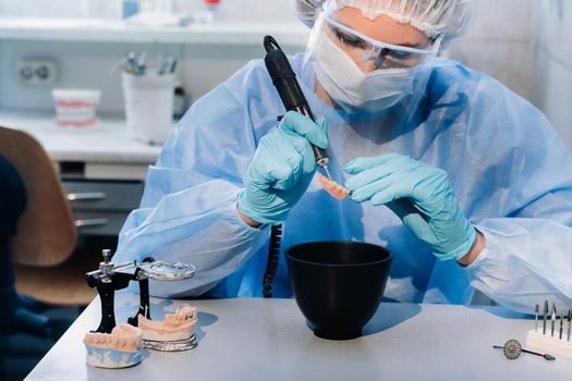 A masked and gloved dental technician works on a prosthetic tooth in his lab.