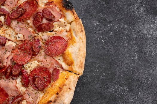 Four meat pizza with meat, sausage, ham and chicken on a dark concrete background