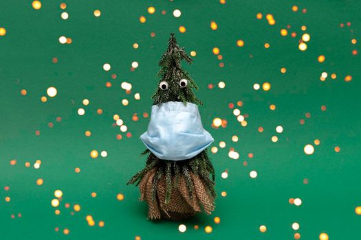 Christmas tree with blue facial medical protective mask and googly eyes on green background, bokeh style, celebration with lockdown due to covid