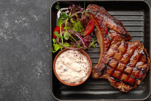 Grilled steak with sauce, vegetables and herbs, on a black frying pan, on a dark background