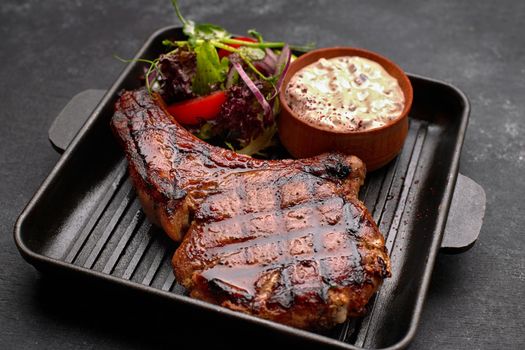 Grilled steak with sauce, vegetables and herbs, on a black frying pan, on a dark background