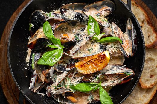 Cooked mussels in a skillet with cheese and basil leaves, on a wooden board, on a dark background