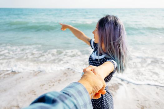 Couple in love resting on summer vacations. Beautiful young woman holding man's hand and pointing at sea, point of view shot. Focus on male hand.