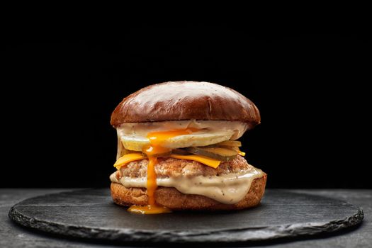 Burger with egg, meat cutlet and cheese on a black background