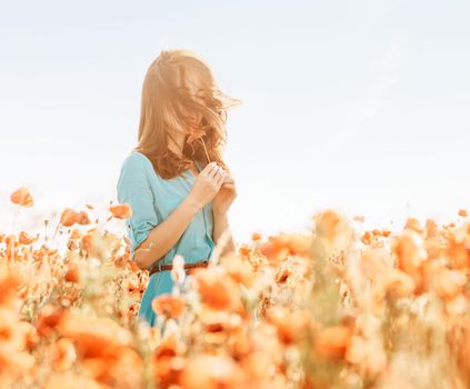 Beautiful young woman standing in poppies meadow and sniffing a flower in summer outdoor.