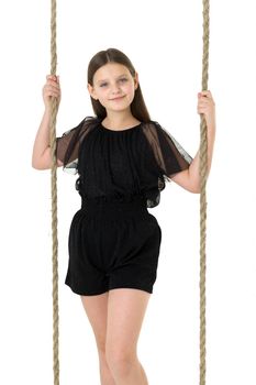 Joyful girl swinging on rope swing. In Stylish Jumpsuit