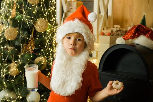 Kid Santa Claus takes a cookie on Christmas Eve as a thank you gift for leaving presents to a grateful boy or girl. Santa picking cookie. Santa picking cookie and glass of milk at home