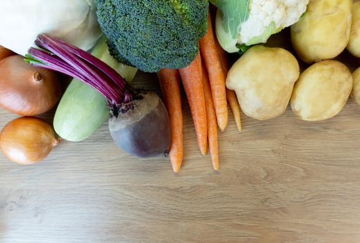Different fresh vegetables, potatoes, carrots, cauliflower, broccoli, beet, zuccini and onion are on wooden table, view from top, copy space, good background.