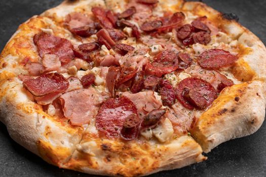 Four meat pizza with meat, sausage, ham and chicken on a dark concrete background