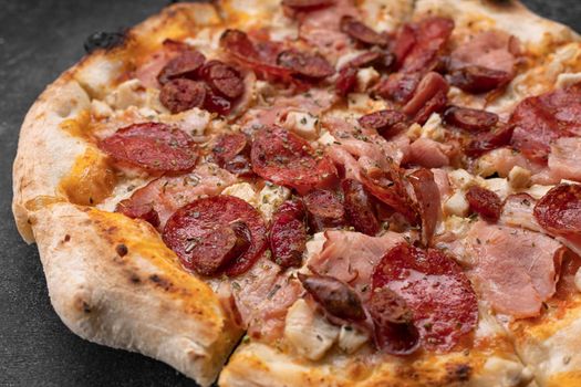 Four meat pizza with meat, sausage, ham and chicken on a dark concrete background