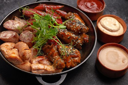 Meat set for beer, sausage, ribs, grilled wings, and three sauces, on a black background