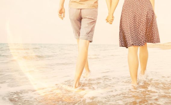 Unrecognizable young loving couple walking on sea coast and holding hands, rear view. Image with sunlight effect.