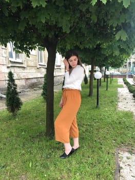 Girl smiling near a flowering tree. Outdoor portrait of a young beautiful fashion lady posing near a blossoming tree. Women's beauty fashion. Girl smiling.