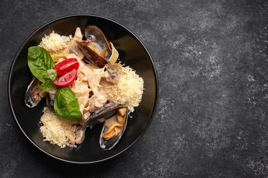 Pasta with seafood, mussels, scallop, rapana and cheese, on a black plate