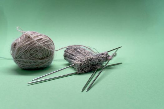 Close up of knitting socks. There are thread and needles on green backgroung. Bright photo.