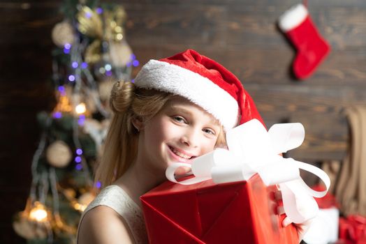 The morning before Xmas. Portrait kid with gift on wooden background. Cute little girl is decorating the Christmas tree indoors