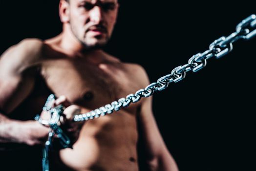 Muscular guy with chains on shoulders against a black background