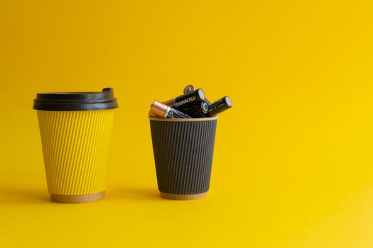 Kiev,Urkaine,16 June 2020,Two takeaway paper coffee cups,yellow with coffee and plastic cover,black cup with Duracell AA batteries,association of energy,yellow background,creative idea,space for text.