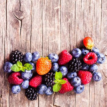 Summer wild berries over shabby wooden background. Raspberry, strawberry, blackberry and blueberry on the table