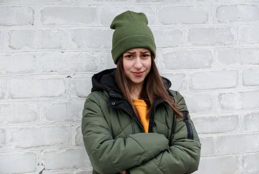 Portrait of a beautiful shy smiling girl in a yellow sweater and khaki hat, which stands near a white brick wall. The concept of emotions and copy space