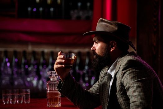 Attractive bearded man in whiskey bar. Hipster with beard and mustache in suit drinks alcohol after working day