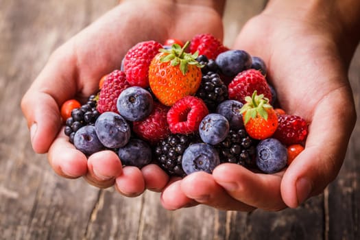 Summer wild berries in hands - raspberry, strawberry, blackberry and blueberry