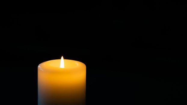 Burning candle on dark background, space for text. Symbol of sorrow.