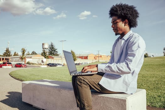 Side view of afro man working in laptop in bench park