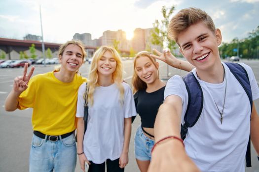 Smiling group of teenagers taking selfie, happy four teens looking at camera, city urban background. Fun, friendship, lifestyle, leisure, summer, adolescence, students concept
