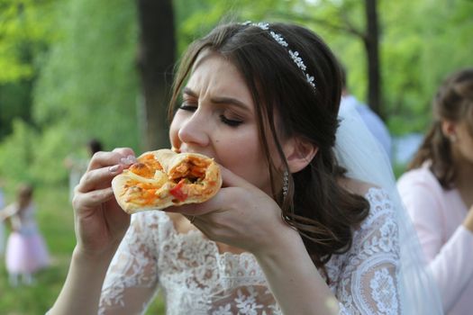 Wedding photo bride eats pizza outdoors in the forest.