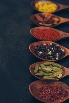 Various spices in wooden spoons on old black table