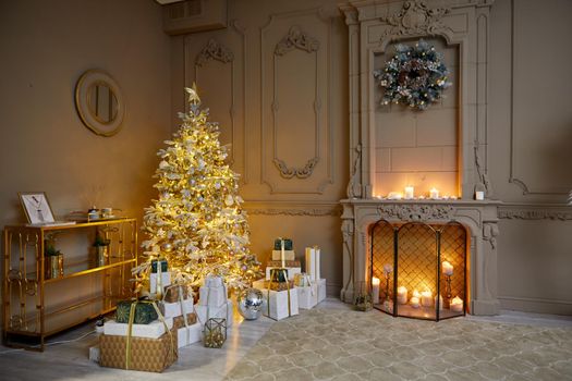Room decorated to christmas celebration studio. White Christmas tree with white and gold balls in a dark room with a decorative fireplace and candles among boxes with gifts