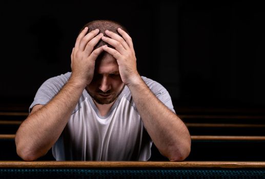 A Sad Christian man in white shirt is sitting and praying with humble heart in the church.