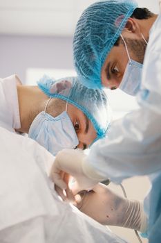 Two surgeons in blue robes make operation in surgery room, close up