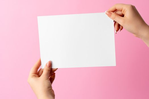 Woman hand showing blank business card on pink background. Close up.