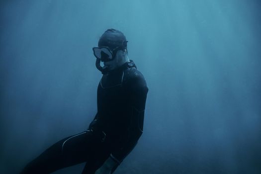 Man in wetsuit and mask swimming underwater in blue deep sea.