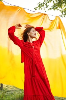 pretty woman in red dress yellow fabric on nature background. High quality photo