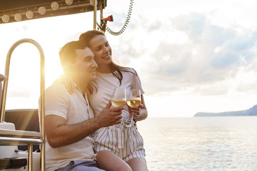 Young loving couple sitting on the yacht deck and drinking wine together