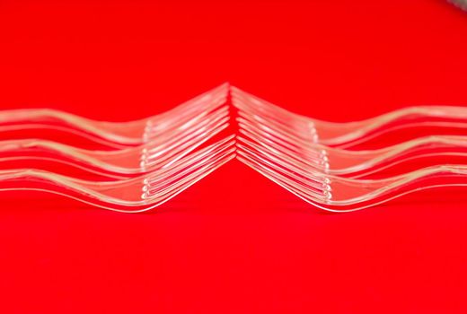 Close-up of clear plastic fork on a red background. Disposable tableware pattern.