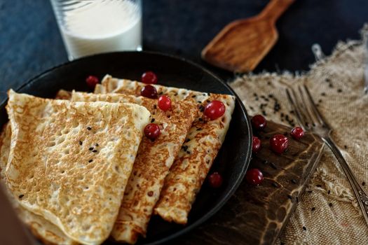 Delicious home-cooked food. Pancakes in a frying pan with cranberry berries and milk. National Russian cuisine. Ready lunch. Rustic style.