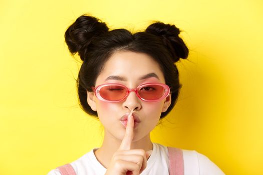 Summer fashion concept. Close-up portrait of glamour asian woman in sunglasses telling a secret, asking be quiet, making hush taboo sign and winking at camera.