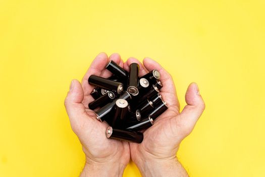 Pile of black aa batteries in mans handful on yellow background, view from the top, minimal concept, copy space.