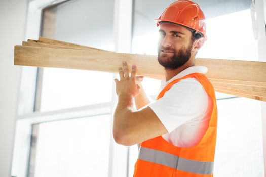 Builder man in hardhat carrying timber on building site, close up portrait