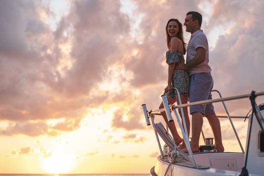 Beautiful loving couple looking at sunset from the yacht