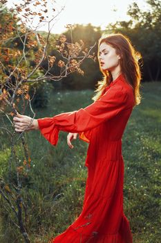 woman in red dress in field near tree posing summer. High quality photo