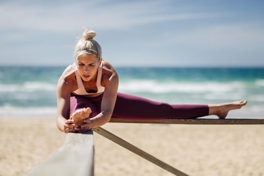 Caucasian woman practicing yoga at seashore. Young female stretching legs in the beach in Cadiz, Andalusia, Spain.